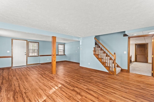 unfurnished living room with stairs, a textured ceiling, baseboards, and light wood-style floors