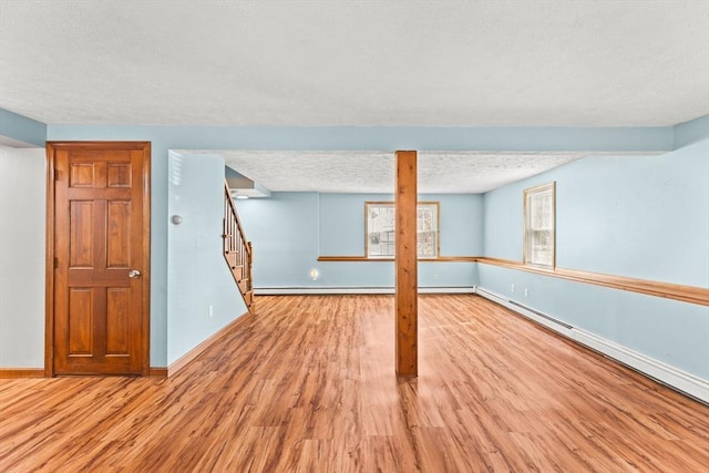 basement featuring a textured ceiling, a baseboard radiator, wood finished floors, baseboards, and stairway