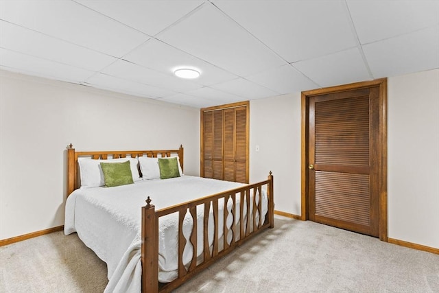 carpeted bedroom featuring baseboards and a drop ceiling