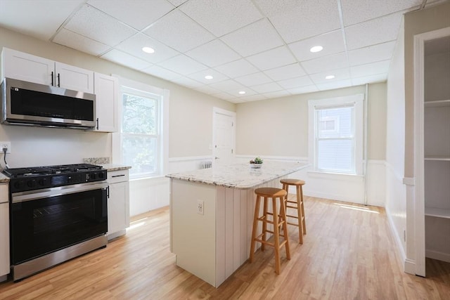 20-22 Ashland Ave, Methuen, MA 01844 - kitchen with stainless steel microwave, range with gas stovetop, a wainscoted wall, a breakfast bar area, and light wood finished floors