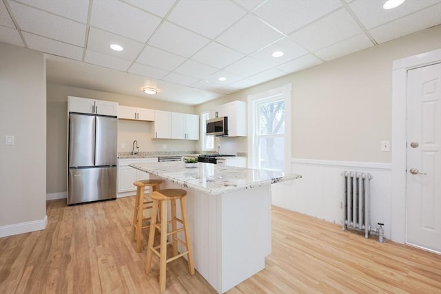 20-22 Ashland Ave, Methuen, MA 01844 - kitchen featuring stainless steel appliances, radiator, a paneled ceiling, a kitchen breakfast bar, and white cabinetry