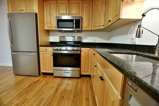 kitchen featuring dark stone counters, sink, stainless steel appliances, and light hardwood / wood-style floors