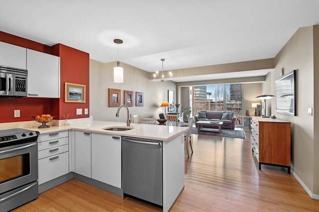 kitchen with stainless steel appliances, a peninsula, a sink, open floor plan, and light countertops