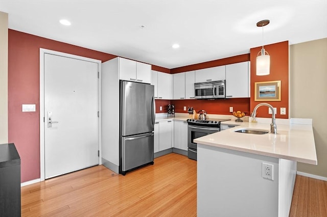 kitchen with light countertops, appliances with stainless steel finishes, white cabinets, a sink, and a peninsula