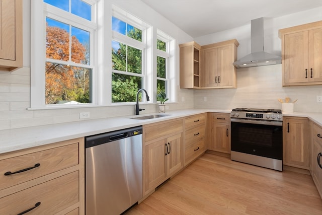 kitchen with wall chimney range hood, light hardwood / wood-style flooring, sink, light brown cabinetry, and appliances with stainless steel finishes