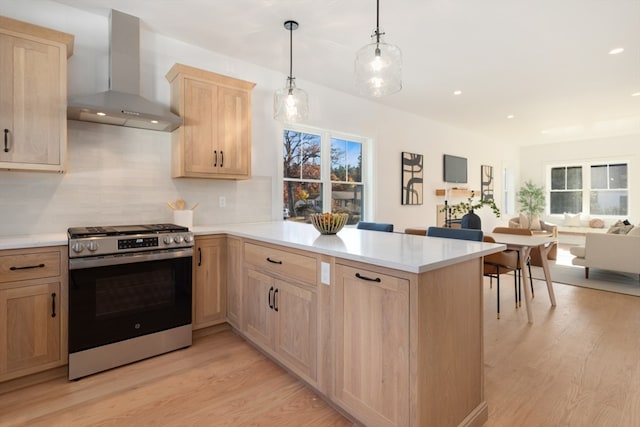 kitchen featuring gas stove, wall chimney exhaust hood, light hardwood / wood-style flooring, and kitchen peninsula