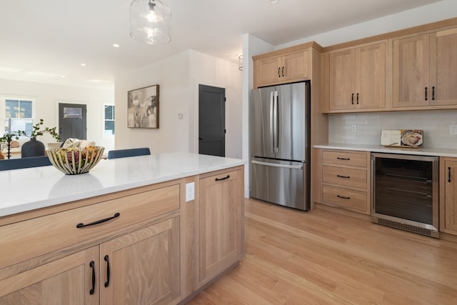 kitchen featuring hanging light fixtures, beverage cooler, stainless steel refrigerator, light hardwood / wood-style flooring, and light brown cabinets