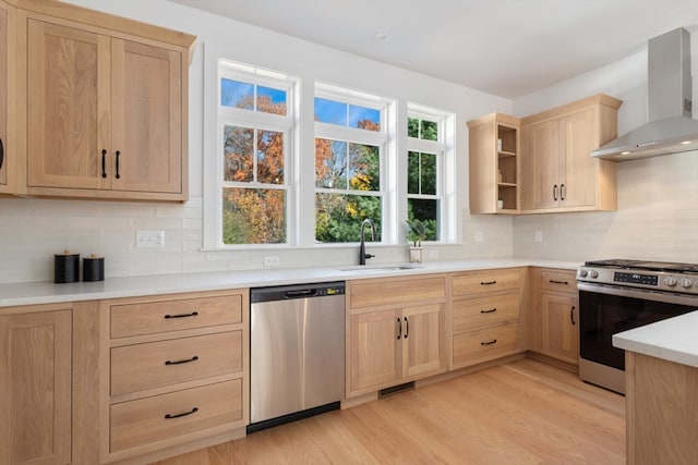 kitchen with wall chimney range hood, light hardwood / wood-style flooring, sink, light brown cabinetry, and appliances with stainless steel finishes