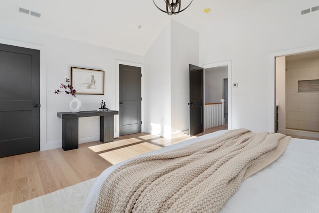 bedroom featuring a notable chandelier, ensuite bath, high vaulted ceiling, and light wood-type flooring