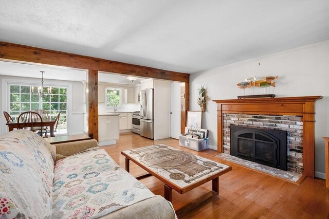 living room featuring an inviting chandelier, sink, a brick fireplace, and light hardwood / wood-style floors