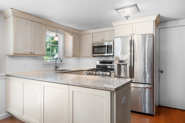 kitchen featuring wood-type flooring, stainless steel appliances, sink, light stone counters, and kitchen peninsula