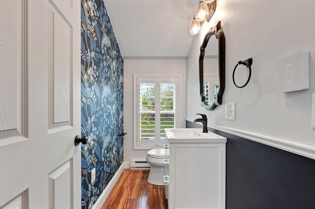 bathroom with wallpapered walls, baseboard heating, wood finished floors, toilet, and vanity