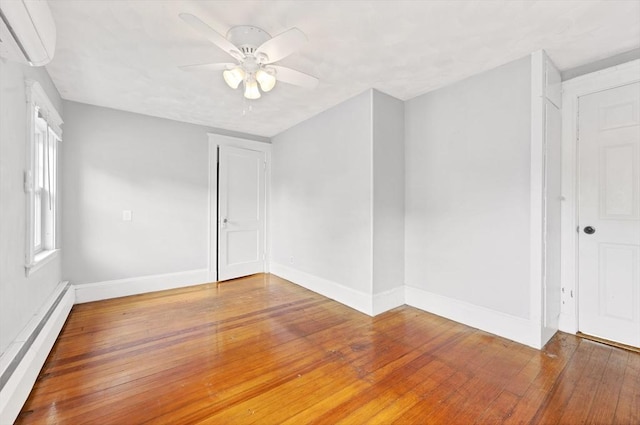 empty room featuring baseboard heating, ceiling fan, a wall unit AC, and hardwood / wood-style floors