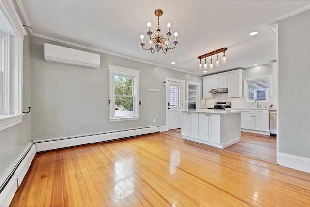 kitchen with a wall mounted air conditioner, stainless steel appliances, under cabinet range hood, baseboard heating, and crown molding