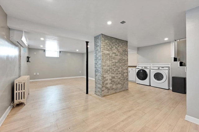 clothes washing area featuring a wall mounted air conditioner, washer and dryer, radiator heating unit, light wood-style flooring, and baseboards