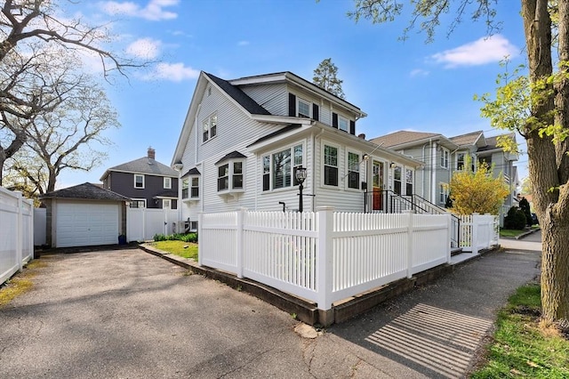 view of front of house with fence, an outdoor structure, a detached garage, and asphalt driveway