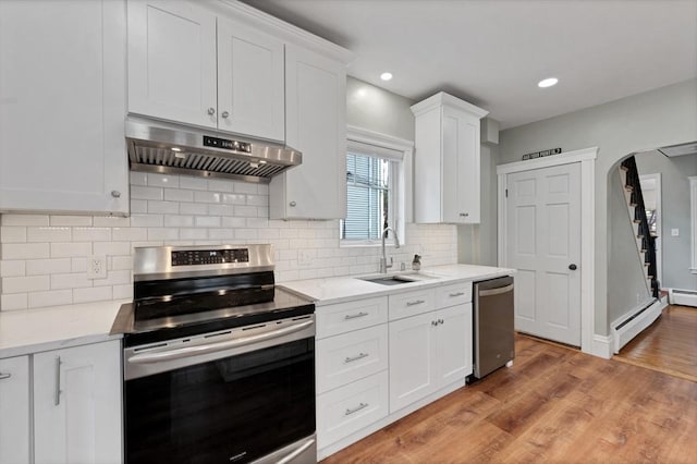 kitchen featuring appliances with stainless steel finishes, under cabinet range hood, a sink, a baseboard heating unit, and white cabinetry
