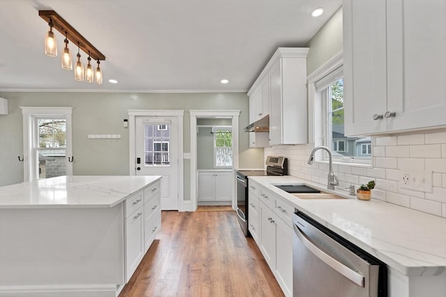 kitchen with appliances with stainless steel finishes, under cabinet range hood, a sink, a kitchen island, and decorative backsplash