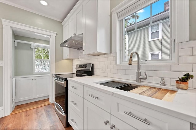 kitchen with stainless steel electric range oven, under cabinet range hood, a sink, light countertops, and white cabinetry