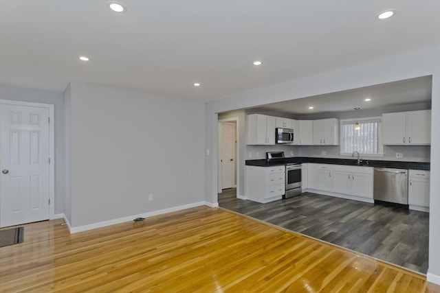 kitchen with dark countertops, dark wood-style floors, stainless steel appliances, a sink, and recessed lighting