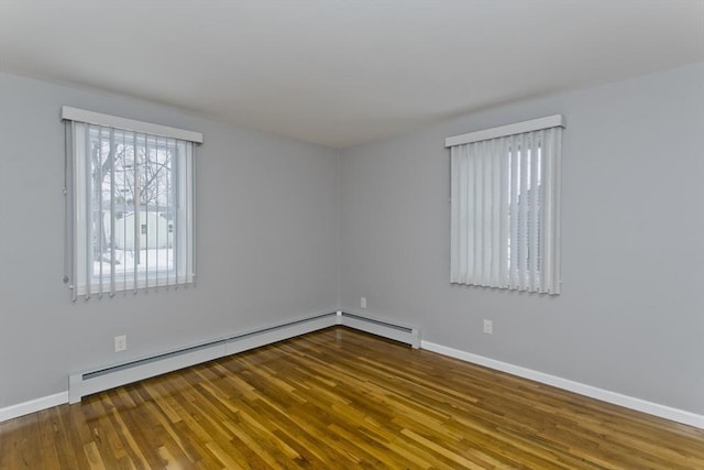 unfurnished room featuring a baseboard heating unit, baseboards, and wood finished floors