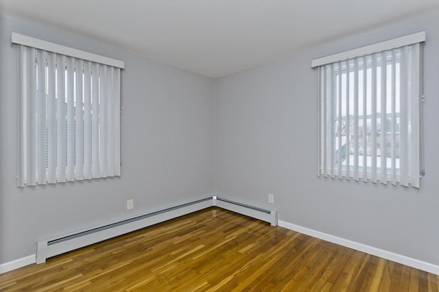 empty room featuring baseboard heating, baseboards, and wood finished floors