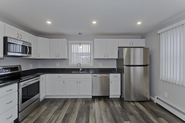 kitchen featuring stainless steel appliances, dark countertops, a baseboard heating unit, white cabinetry, and a sink