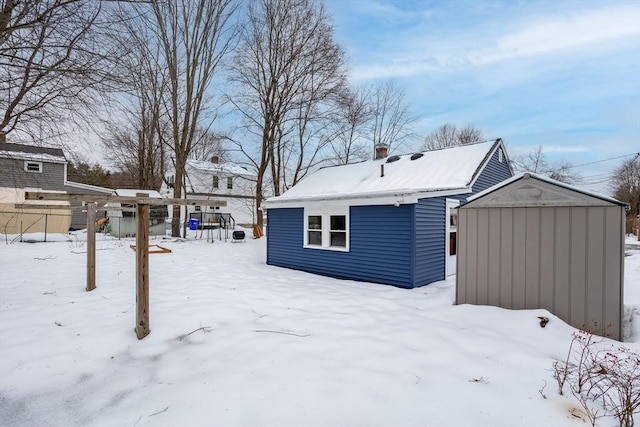 snow covered property featuring an outdoor structure, a storage shed, and fence