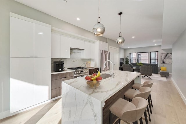 kitchen with a center island with sink, white cabinetry, light stone countertops, and stainless steel appliances