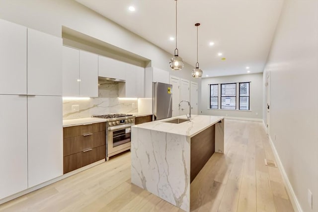 kitchen featuring an island with sink, light stone counters, refrigerator, high end stainless steel range, and white cabinetry