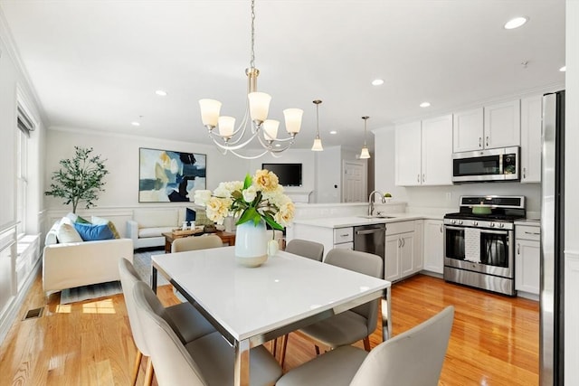 kitchen featuring appliances with stainless steel finishes, crown molding, light wood-type flooring, a chandelier, and white cabinets