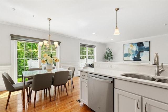 kitchen featuring stainless steel dishwasher, a sink, crown molding, a chandelier, and light countertops