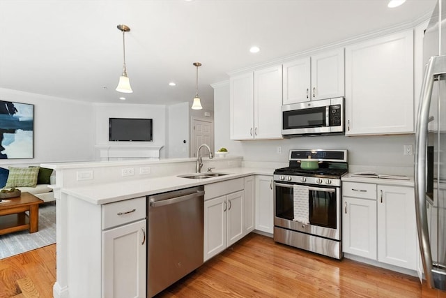 kitchen with stainless steel appliances, a sink, open floor plan, a peninsula, and white cabinetry