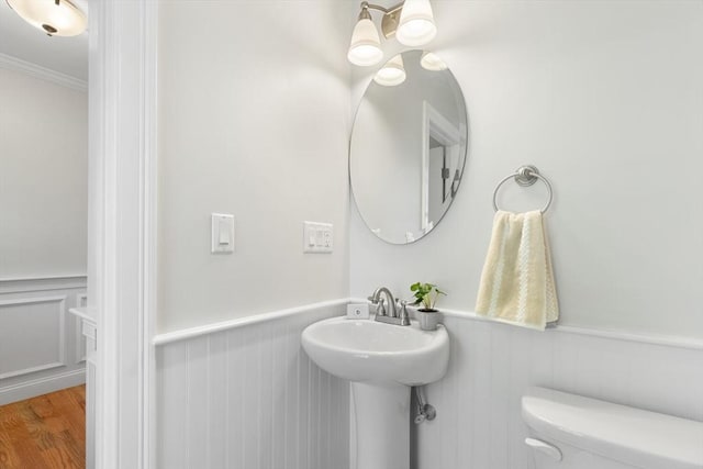 bathroom featuring a wainscoted wall, toilet, wood finished floors, ornamental molding, and a sink