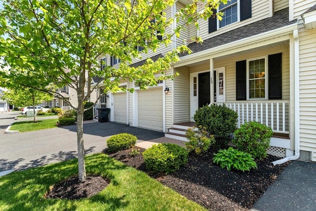 entrance to property with roof with shingles, an attached garage, covered porch, and asphalt driveway
