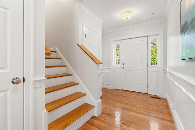 foyer featuring stairway, light wood-type flooring, ornamental molding, and a wainscoted wall