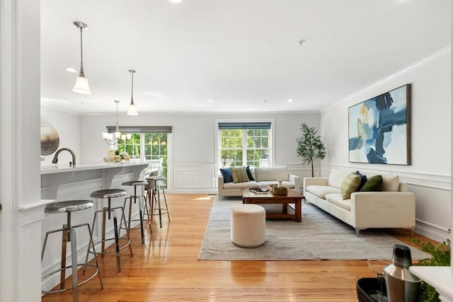living room with crown molding, light wood-type flooring, a decorative wall, recessed lighting, and wainscoting