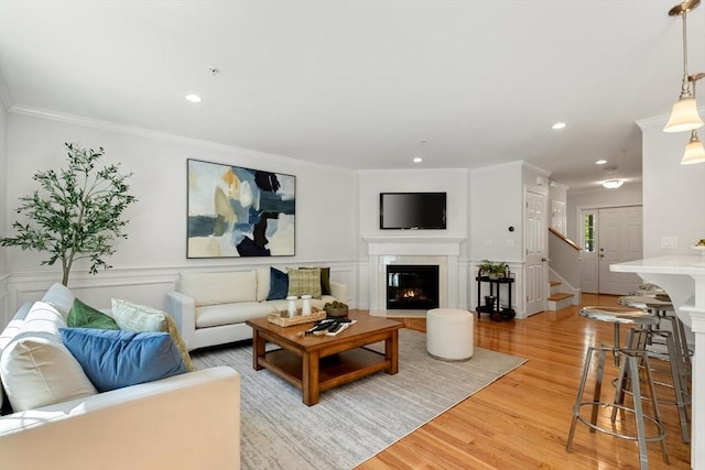 living area with a glass covered fireplace, light wood-style floors, ornamental molding, stairs, and recessed lighting
