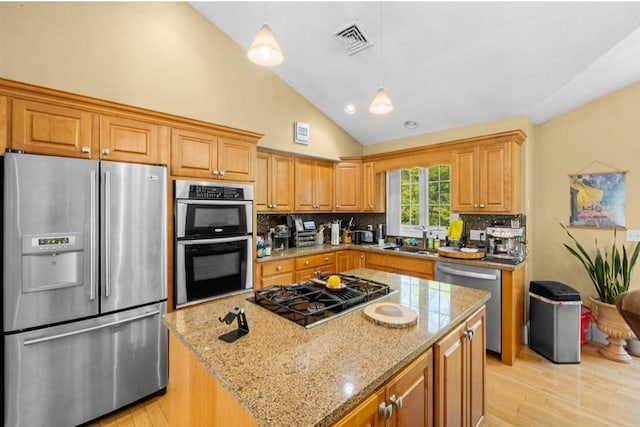 kitchen featuring appliances with stainless steel finishes, a sink, light wood-style flooring, light stone counters, and decorative backsplash