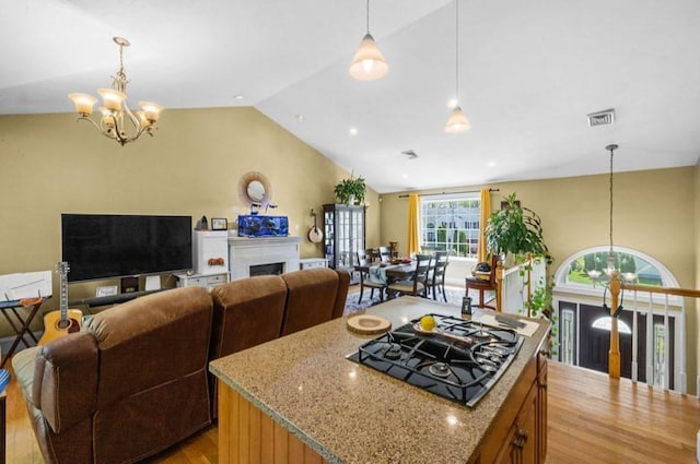 kitchen featuring a chandelier, black gas stovetop, vaulted ceiling, light stone counters, and a fireplace