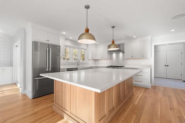 kitchen featuring white cabinets, appliances with stainless steel finishes, hanging light fixtures, a large island, and light hardwood / wood-style flooring