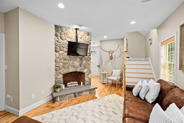living room featuring baseboards, stairway, wood finished floors, and a stone fireplace