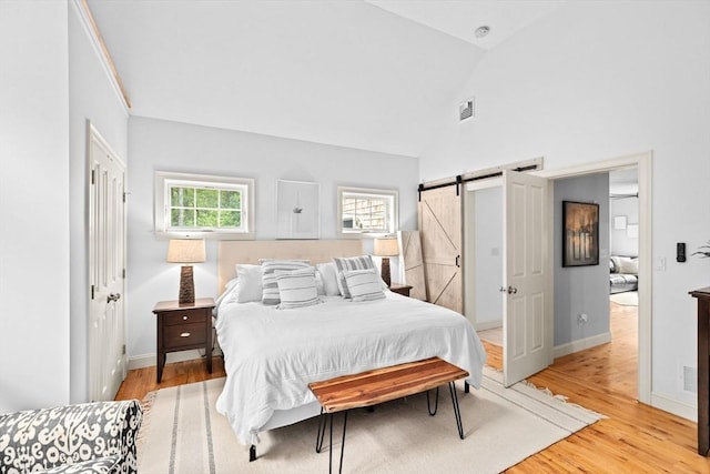 bedroom featuring a barn door, light wood-style flooring, baseboards, and high vaulted ceiling