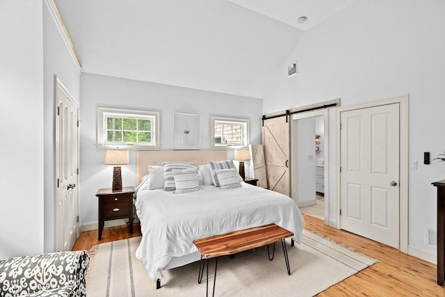 bedroom with a barn door, light wood-style floors, high vaulted ceiling, and baseboards