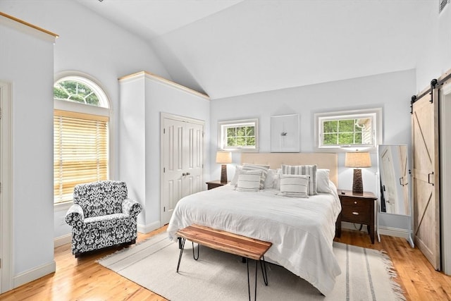 bedroom featuring a barn door, multiple windows, vaulted ceiling, light wood-style floors, and a closet
