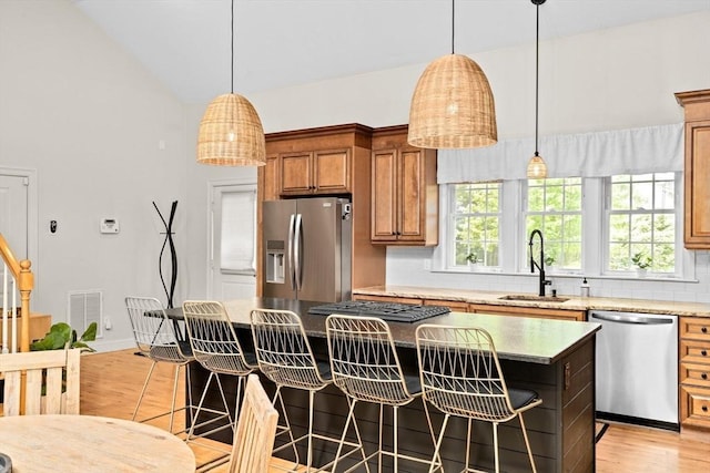 kitchen with stainless steel appliances, a sink, brown cabinets, light wood-style flooring, and backsplash