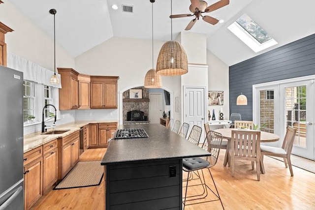 kitchen with a sink, high vaulted ceiling, appliances with stainless steel finishes, brown cabinetry, and a ceiling fan