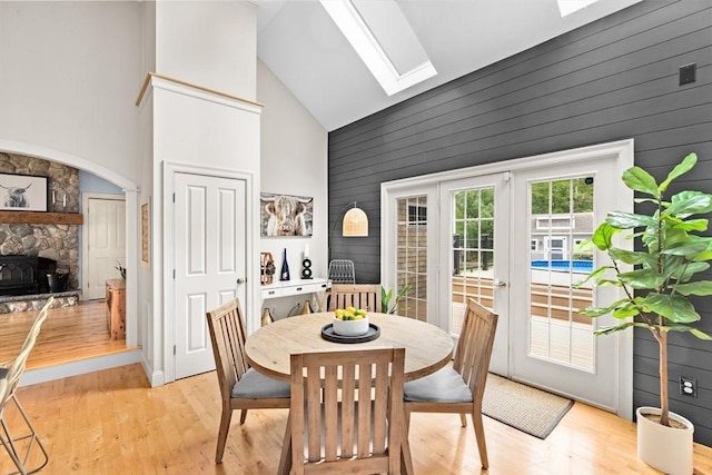 dining space with high vaulted ceiling, a skylight, light wood-style flooring, wood walls, and a fireplace