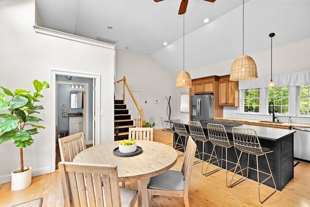 dining space with stairs, light wood-type flooring, baseboards, ceiling fan, and high vaulted ceiling