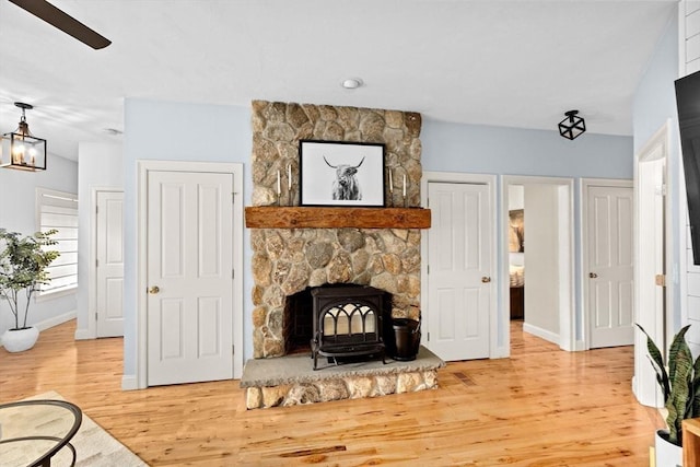 living area featuring a wood stove, light wood-style floors, baseboards, and ceiling fan